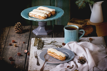Old wooden Christmas table with Butter cream Eclairs and mug of hot tea, decorating by Christmas stars, tree and vintage books. With open old door at bachground. Dark rustic style, outside viewの写真素材