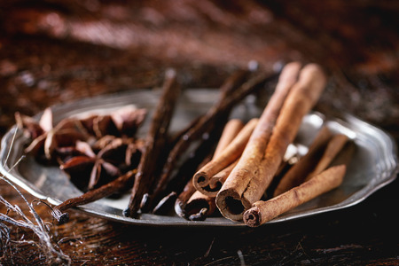 Heap of spices cinnamon sticks, vanilla sticks and anise stars in vintage metal plate over dark palm crust.の写真素材