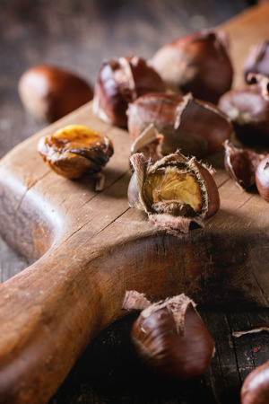 Close up of peeled  and unpeeled grilled edible chestnuts on vintage cutting board over old wooden tableの写真素材