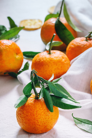 Heap Tangerines with leaves and dry sliced orange on white textile surface. Side viewの写真素材