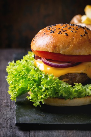 Fresh homemade hamburger with black sesame seeds on black slate board with fried potatoes, served with sea salt over old wooden table with dark background. Dark rustic style.の写真素材