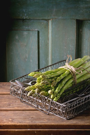 Green asparagus and cutlery in vintage metal grid box over wooden table with turquoise wooden background. Dark rustic atmosphereの写真素材