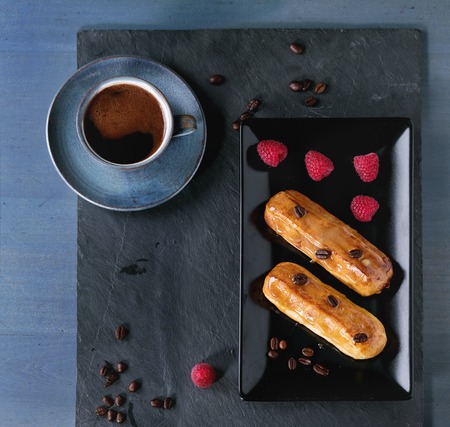 Ceramic plate with Coffe eclairs with cup of fresh black coffee, raspberries and coffee beans on...