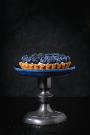 Lemon tartlet with fresh blueberries, served on vintage cake stand over black background.の写真素材