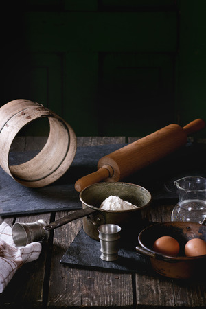 Ingredients for dough making. Flour, eggs in vintage copper bowls and salt with sieve and rolling-pin over old wooden table. Rustic style.の写真素材