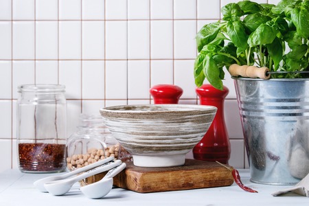 Fresh herbs Basil and Parsley in metal pots and ceramic bowl of raw chick-pea over kitchen table...