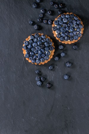 Two Lemon tartlets with fresh blueberries over black stone slate background. Top view. With space for textの写真素材