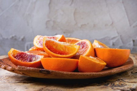 Sliced Sicilian Blood oranges fruits in brown clay plate over natural stone background.