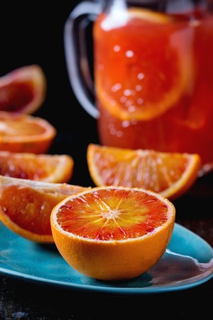 Sliced Sicilian Blood oranges in turquoise ceramic plate and glass mason jar of fresh red orange juice over old wooden table. Dark rustic style.の写真素材