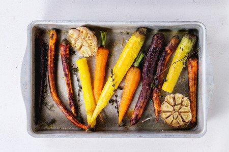 Baked whole colorful carrots with garlic and thyme in vintage aluminum tray over old wooden surface. Top viewの写真素材