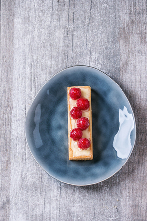Square Tartlet with custard and fresh glazed raspberries, served on gray ceramic plate over white...