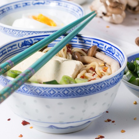 Chinese porcelain bowl of asian ramen soup with feta cheese, noodles, spring onion and mushrooms,...