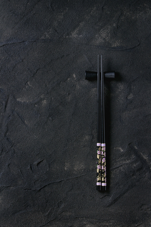 Black painted chopstics and chopsticks rest over black textured surface. With copy space. Top view.の写真素材