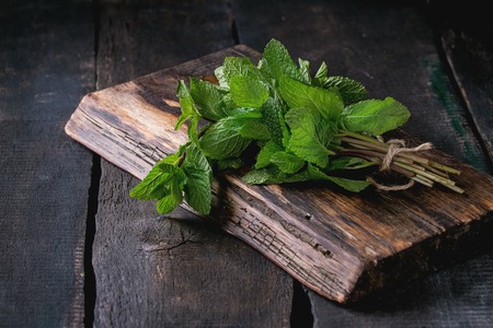 Bunch of fresh mint with thread on wooden chopping board over old wooden background. Dark rustic styleの写真素材