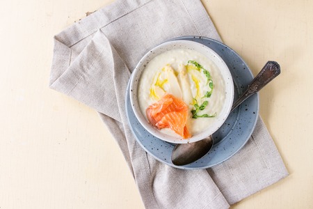 Bowl of white asparagus cream soup with pea sprouts, salted salmon and toast on gray textile napkin over white wooden background. Flat lay with copy spaceの写真素材