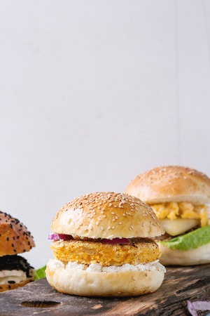 Three Homemade veggie burgers with sweet potato, black rice and red beans, served on wooden chopping board with kitchen towel over white textured background.の写真素材
