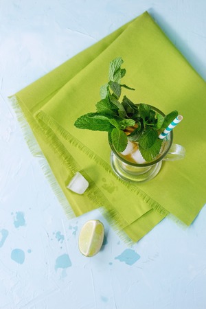 Glass of Iced green tea with lime, lemon, mint and ice cubes on green textile napkin over light blue textured background. Flat layの写真素材