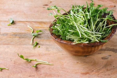 Wooden Bowl of pea sprouts over textured wooden background.