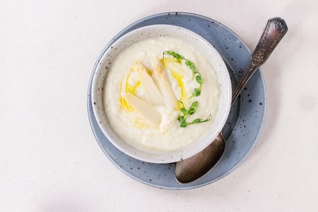 Bowl of white asparagus cream soup with pea sprouts over white stone background. Flat lay with copy spaceの写真素材