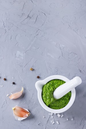 Homemade ramson green pesto sauce in white ceramic mortar with pestle over gray textured background with sea salt, pepper ang garlic. Top view with copy spaceの写真素材