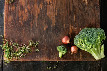 Wooden healthy food background with raw vegetables and herbs. Onions, broccoli and thyme over wooden textured surface. Flat lay. Copy space for text.の写真素材