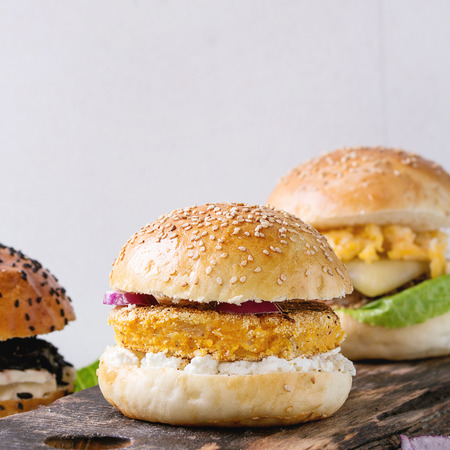 Three Homemade veggie burgers with sweet potato, black rice and red beans, served on wooden chopping board with kitchen towel over white textured background. Square imageの写真素材