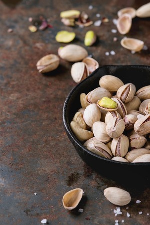 Salted roasted pistachios nuts with shell and salt  in  in black small cast-iron pan over old rusty iron textured background. With copy spaceの写真素材