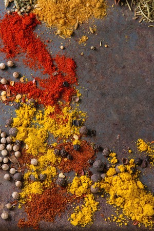 Spicy background with assortment of different hot chili and allspice peppers and mix of other spices over old rusty iron background. Top view. With space for textの写真素材