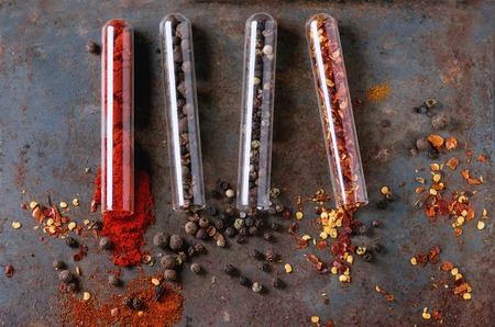 Spicy background with assortment of different hot chili and allspice peppers in glass test-tube over...