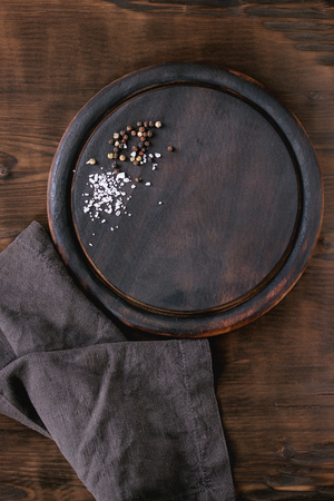 Round wood Chopping cutting board, seasoning peppers and sea salt on gray textile napkin over dark wooden background. Top view with copy spaceの写真素材