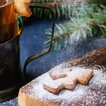 Shortbread Christmas cookies for cups in sugar powder, glass of hot tea in cup holder on table with blue tablecloth. Cookies Shapes as Christmas tree with sifting powder. Square imageの写真素材