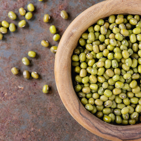 Healthy superfood. Uncooked green mungo beans in olive wood bowl over old rusty iron background. Top view. Close up. Square imageの写真素材