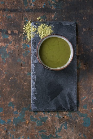 Ceramic cup of green matcha tea with glass teapot with hot water on black slate board over dark wooden textured background. Healthy food. With copy space. Top viewの写真素材