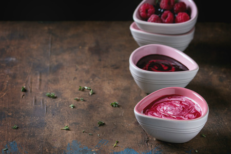 Three pink ceramic bowls of berry dessert soups, cream and fresh blueberry and raspberry, served over old wood textured background. Summer healthy eating theme. With copy spaceの写真素材