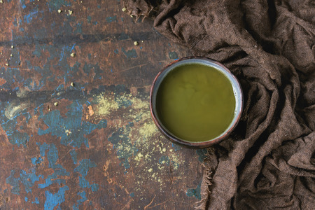 Ceramic cup of green matcha tea on wet sackcloth rag over dark wooden textured background. Healthy food. With copy space. Top viewの写真素材