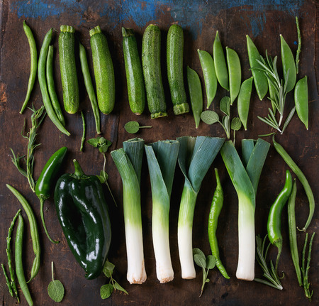 Assortment of fresh raw green vegetables baby leek, zucchini, beans, sweet peas, green paprika, hot chili peppers and herbs over old wood textured background. Top viewの写真素材