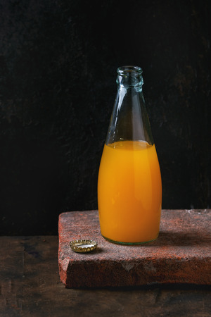 Opened glass bottle of citrus orange and lemon lemonade, standing with iron cap on clay stone board over black background. With copy spaceの写真素材