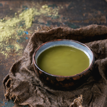 Ceramic cup of green matcha tea on wet sackcloth rag over dark wooden textured background. Healthy food. With copy space. Square imageの写真素材