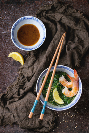 Chinese bowls with Cooked spinach and fried shrimps prawns with lemon and sesame seeds, soy sauce and chopsticks on sackcloth over old iron background. Asian style dinner. Top viewの写真素材