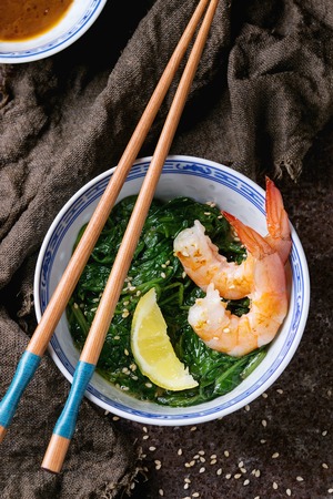 Chinese bowls with Cooked spinach and fried shrimps prawns with lemon and sesame seeds, soy sauce and chopsticks on sackcloth over old iron background. Asian style dinner. Top viewの写真素材