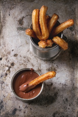 Traditional spanish treat churros with chocolate sauce, served in tin can over old textural metal...