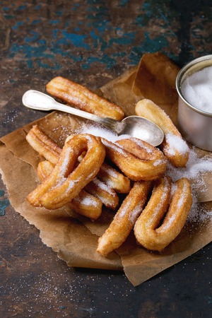 Traditional spanish treat churros with granulated sugar, served on baking paper with tin can of sugar oval plate over dark wooden background. Copy spaceの写真素材