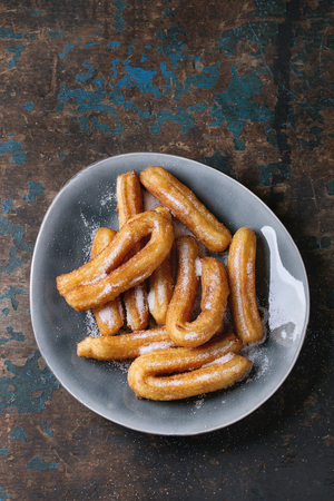 Traditional spanish treat churros with granulated sugar, served in gray oval plate over dark wooden background. Top view with copy spaceの写真素材