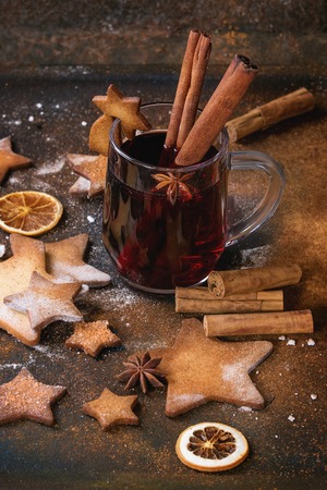 Glass mug of hot red mulled wine spices, sugar shortbread cookies star shape and cookie on glass, anise and cinnamon powder over dark textured background. Christmas drink treat theme.の写真素材