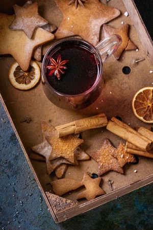Glass mug of hot red mulled wine spices, sugar shortbread cookies star shape, anise and cinnamon powder in wooden box over dark texture background. Christmas drink treat. Overhead viewの写真素材