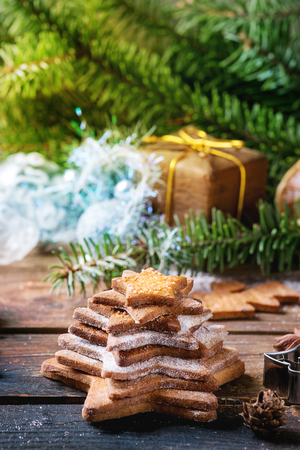 Stack of homemade Christmas shortbread star shape sugar cookies different size with sugar powder on old wooden surface with Christmas decor and fir tree at background.の写真素材