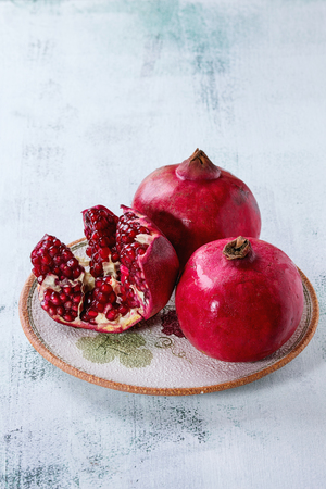 Ripe slice and whole pomegranates on ornate ceramic plate over white wooden background.の写真素材