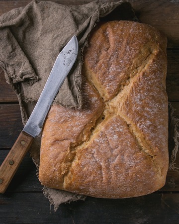 Whole fresh baked artisan bread under sackcloth with vintage knife over old wooden background. Overhead view.の写真素材