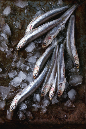 Lot of raw fresh anchovies fishes on crushed ice over old dark metal background. Top view. Sea food background theme.の写真素材