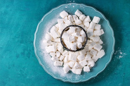 Heap of homemade vanilla marshmallow in old mug on big plate over bright wooden turquoise background. Top view with copy space.の写真素材